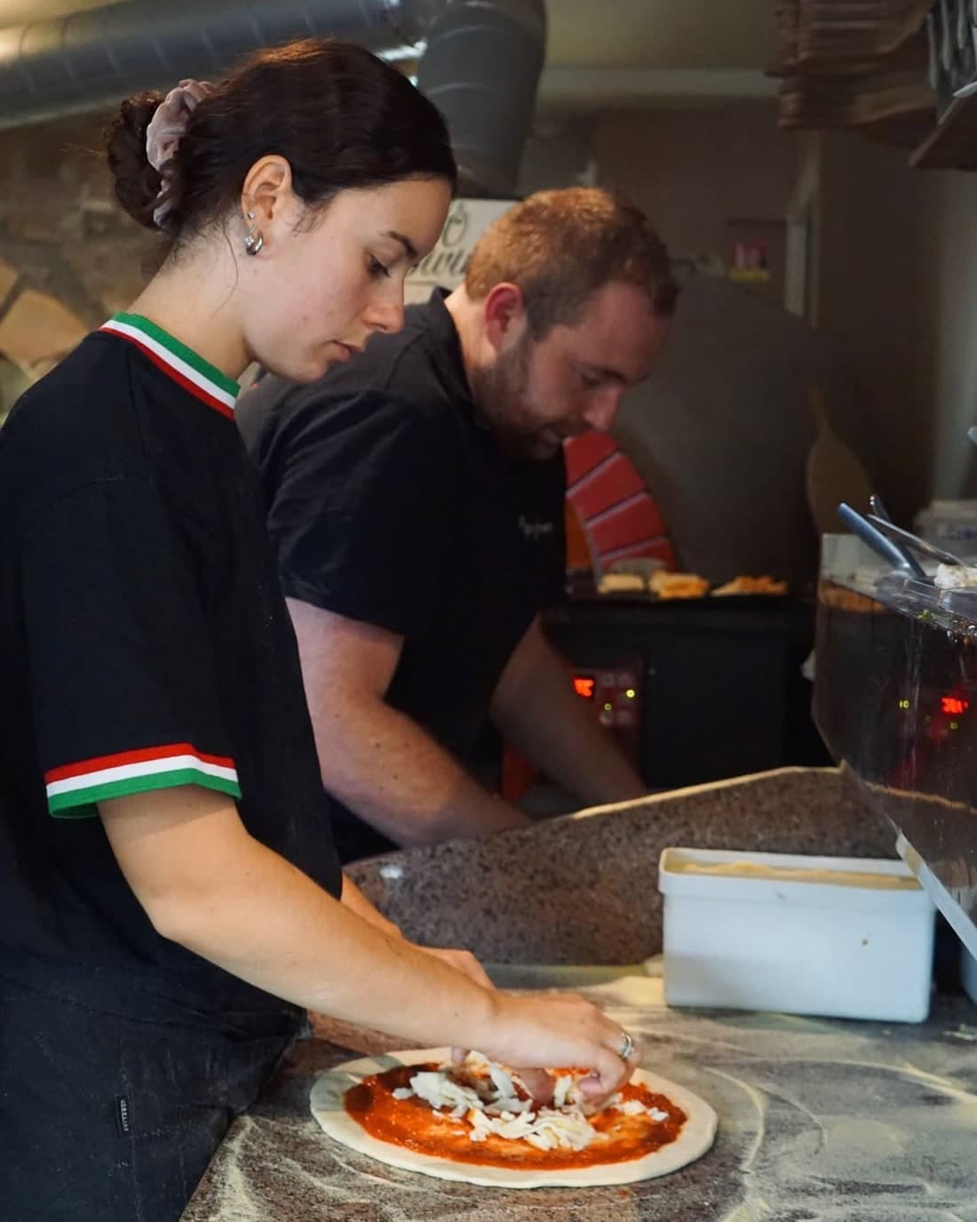 Deux membres de l'équipe préparant des pizzas côte à côte au plan de travail