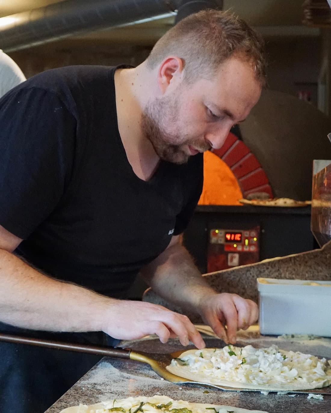 Cuisinier garnissant une pizza sur le plan de travail, devant le four