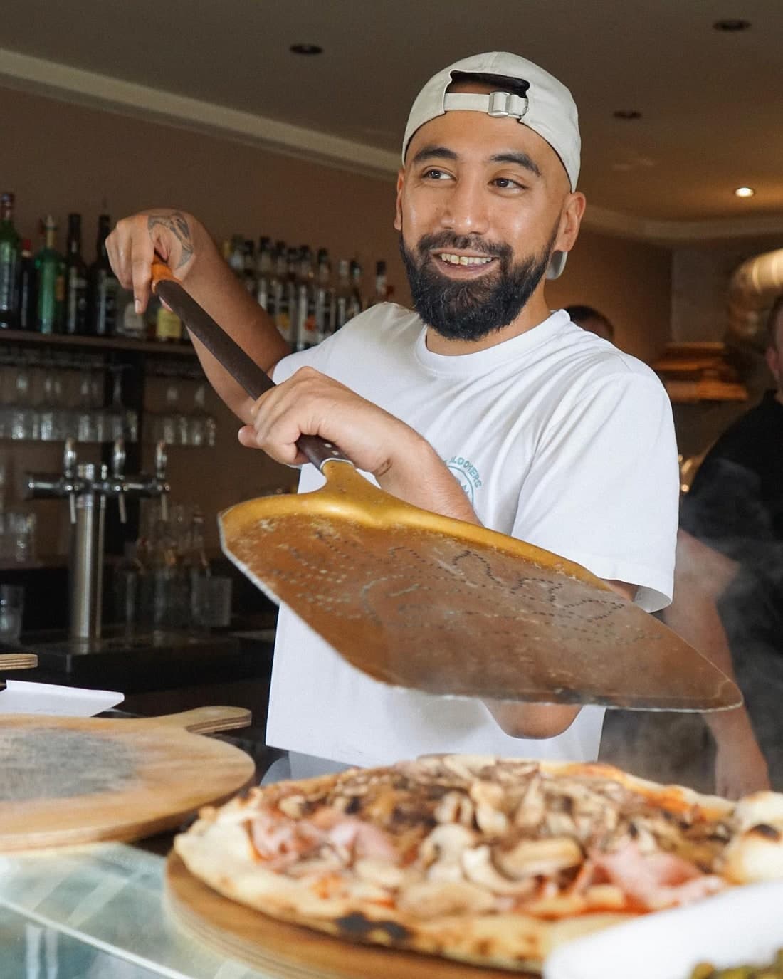 Pizzaïolo souriant, pelle à la main, devant le four à bois d'O'Divino